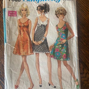 Peut inclure: Pochette de patron de couture Simplicity vintage avec des illustrations de trois robes. L'enveloppe porte le numéro 7988, Junior Taille 9, et Tour de poitrine 81 cm. Les robes sont orange, noir et blanc, et à motifs floraux.