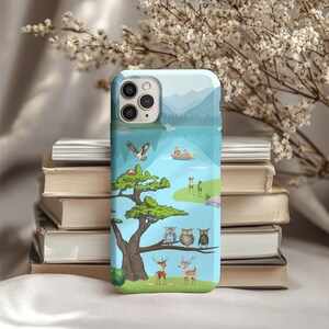 Könnte beinhalten: Eine hellblaue Handyhülle mit einer Naturszene mit See, Bergen und einem Baum mit Eulen und Hirschen. Ein Adler fliegt über einem Boot mit Menschen. Die Hülle liegt auf einem Stapel Bücher.