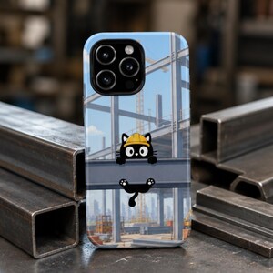 Op de afbeelding: Een smartphonehoesje met een afbeelding van een zwarte kat met een gele veiligheidshelm, hangend aan een stalen balk. De achtergrond toont een bouwplaats met stalen balken, een kraan en een stadssilhouet onder een blauwe lucht.