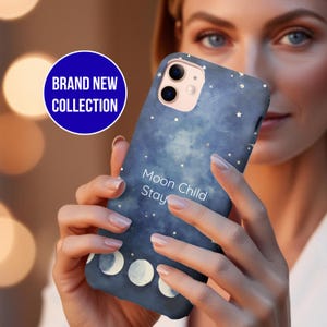 May include: A dark blue phone case with a celestial design, featuring white stars and moon phases. The case has the words "Moon Child Stay" and is part of a "Brand New Collection".