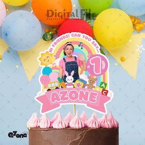 Op de afbeelding: Een chocoladetaart met roze glazuur, bekroond met een taartdecoratie. De topper bevat een regenboog, een stripfiguur en het woord "AZONE". Kleurrijke ballonnen staan op de achtergrond.