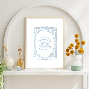 May include: A framed print featuring a blue illustration of an open clam shell with a pearl inside. The artwork is set within an oval frame with decorative flourishes and a bow at the top. The text "Matthew 13:45" is at the bottom.