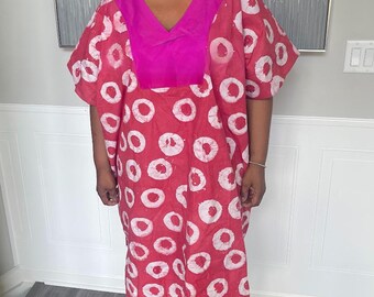May include: A red and white patterned dress with a V-neckline and short sleeves. The dress features a pink yoke and is knee-length. The person is wearing gold platform sandals and gold earrings. The dress has a pattern of white circles on a red background.