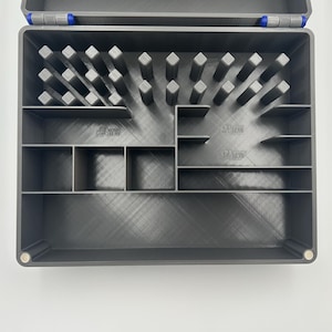 May include: A gray plastic organizer box with multiple compartments and dividers. The box has a hinged lid with blue accents and is designed to hold small items. The interior features various slots and shelves for organization.