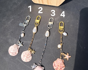May include: Four keychains with seashell charms, pearls, and starfish accents. The keychains have silver and gold-toned hardware. The seashells are pink and white. The keychains are numbered 1, 2, 3, and 4.