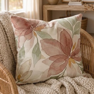 May include: A square throw pillow featuring a watercolor-style floral pattern in muted shades of dusty rose, sage green, and cream. The design displays large, overlapping petals and leaves across the fabric surface, creating a soft, layered botanical aesthetic.