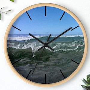 May include: Round wall clock with a light wood frame. The clock face features a photograph of ocean waves under a blue sky. Black hands and hour markers complete the design. A decorative accent for any room.