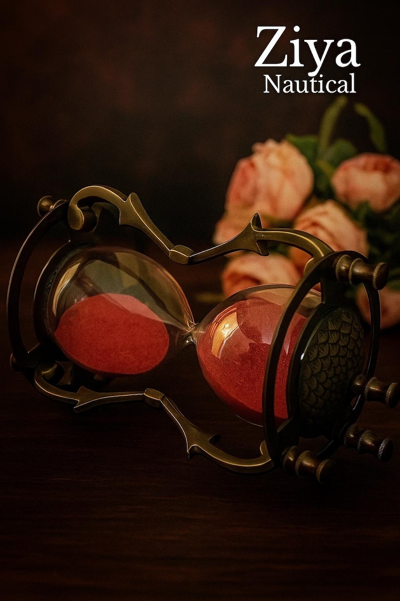 May include: An antique hourglass with a bronze frame and red sand. The glass bulbs are connected by a decorative metal frame. The text "Ziya Nautical" is displayed at the top. The background is dark with a blurred floral arrangement.