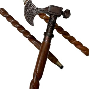 May include: A decorative walking cane with a dark brown, twisted wooden shaft. The top features a metal axe head with ornate detailing and a hammer. The cane is approximately 36 inches long.