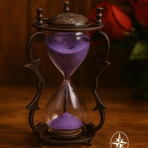 Puede incluir: Un reloj de arena ornamentado con un marco de metal bronce oscuro y bombillas de vidrio transparente llenas de arena púrpura. El reloj de arena tiene un diseño elaborado y el texto "ZIYA NAUTICAL" es visible.