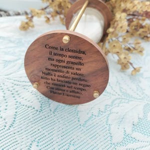 May include: A wooden hourglass with brass detailing and a glass bulb filled with white sand. The base of the hourglass has engraved Italian text. A decorative item.