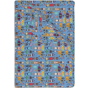 Puede incluir: Una manta azul con un patrón repetitivo de personajes y objetos de dibujos animados coloridos. El diseño incluye figuras, cámaras y otros elementos caprichosos. La manta está doblada, mostrando el patrón en la parte superior y el borde.