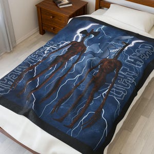 Puede incluir: Una manta azul con un gráfico de dos figuras de Siren Head y rayos. Las palabras "Siren Head" están escritas en blanco. La manta tiene un borde negro. La manta está sobre una cama.