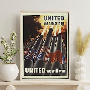 Può includere: Poster vintage incorniciato con il testo "UNITED we are strong" e "UNITED we will win". Il poster presenta razzi con bandiere di diverse nazioni. L'opera d'arte è esposta su una mensola bianca con vasi e piante decorative.