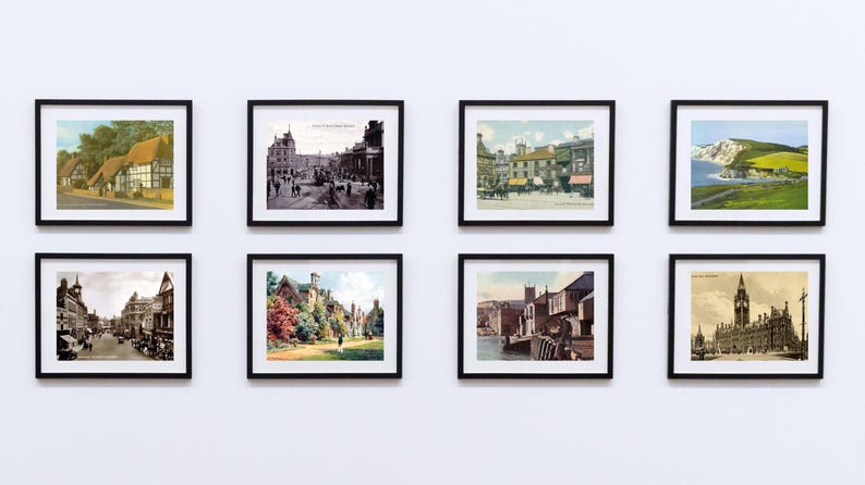 Op de afbeelding: Acht ingelijste vintage prenten van landschappen en architectuur hangen aan een witte muur. De prenten tonen kleurrijke en zwart-wit afbeeldingen van gebouwen, straten en natuurlandschappen. Elke prent zit in een zwart frame.