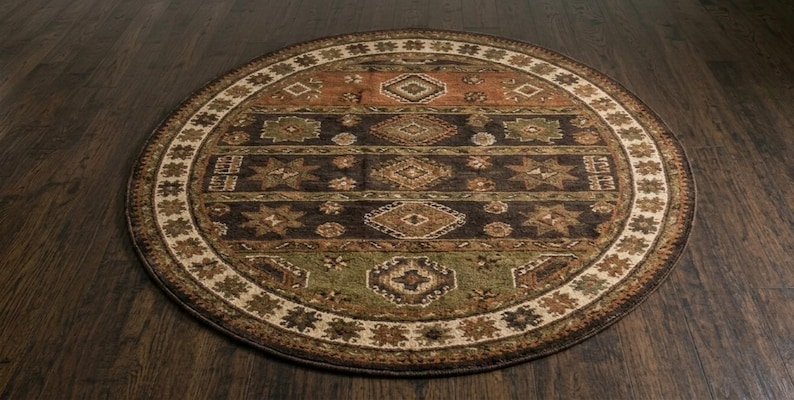 May include: A round area rug featuring a multi-colored geometric pattern with horizontal bands in shades of brown, dark charcoal, and muted green. The border displays a repeating star and diamond motif in cream, tan, and dark brown tones.