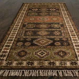 May include: A rectangular area rug featuring a series of horizontal bands in shades of dark brown, olive green, and terracotta. The rug is decorated with repeating geometric diamond and star patterns, finished with a cream-colored border and fringe.