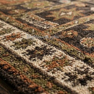May include: A woven rug featuring a dark brown, olive green, and burnt orange geometric pattern with star-like motifs and a textured border. The text "ReWovenCrafts" is visible in the center of the rug, showcasing a dense, knotted pile construction.
