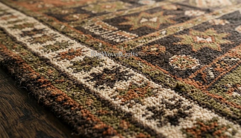 May include: A woven rug featuring a dark brown, olive green, and burnt orange geometric pattern with star-like motifs and a textured border. The text "ReWovenCrafts" is visible in the center of the rug, showcasing a dense, knotted pile construction.