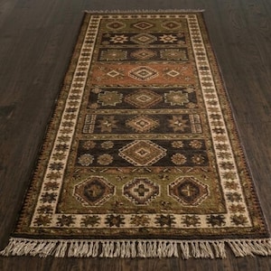 May include: A rectangular runner rug featuring a series of horizontal panels with geometric diamond and star motifs in shades of olive green, dark brown, and terracotta. The rug is framed by a cream border and finished with light beige fringe.