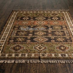 May include: A rectangular area rug featuring horizontal bands in shades of olive green, dark brown, and terracotta orange. The rug displays repeating geometric diamond and star patterns throughout, finished with a cream-colored fringe at both ends.