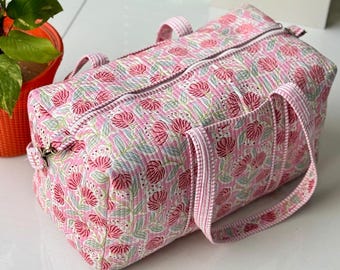 Pode incluir: Mala de viagem rosa com estampa floral. A mala apresenta um design acolchoado com um padrão repetido de flores rosa e folhas verdes sobre um fundo rosa claro. Possui alças combinando e fecho de zíper.