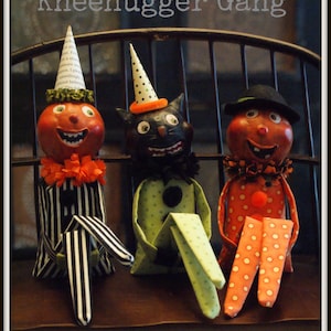 May include: Three vintage-inspired Halloween decorations, a black cat, a pumpkin, and a person, are sitting on a black metal chair. They are all wearing party hats and have a whimsical, handmade look. The text "Vintage Inspired Kneehugger Gang" is at the top of the image, and the text "by cotton pickin' fun!" is at the bottom.