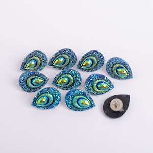 May include: Ten teal blue and green iridescent peacock feather shaped embellishments with a single black button.