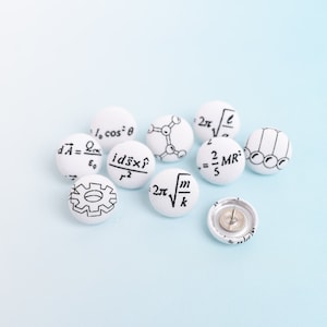 May include: A collection of white push pins with black scientific and mathematical symbols and equations printed on them. One push pin is shown with the pin exposed. The background is a light blue.