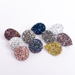 May include: An assortment of sparkling, glittery cabochons in various shapes and colors, including teardrop and round forms. Colors range from silver, gold, and pink to deep blue and purple. These decorative embellishments are ideal for jewelry making and crafts.