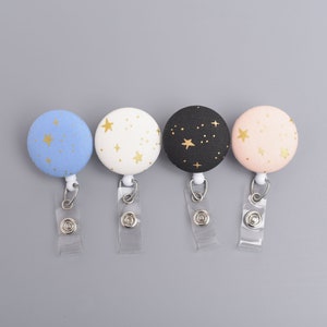 May include: Four different colored round badge holders with gold star patterns. The badge holders are attached to retractable badge reels.