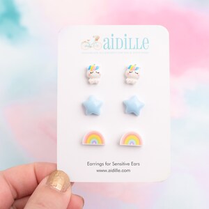 May include: A white card with a set of six colorful earrings. The earrings are shaped like unicorns, stars, and rainbows. The card says "Earrings for Sensitive Ears" and "www.aidille.com".