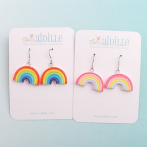 May include: Two pairs of rainbow earrings on white cards with the word "aidille" printed on them. One pair is a traditional rainbow with red, orange, yellow, green, blue, indigo, and violet. The other pair is a pastel rainbow with pink, light blue, yellow, and light green.
