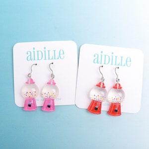 May include: Two pairs of gumball machine earrings. One pair is pink and the other is red. Both pairs have a clear gumball with colorful sprinkles inside.