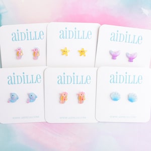 May include: Six cards with the word "aidille" printed on them. Each card features a pair of small, colorful, resin earrings with a sea-themed design. The designs include a seahorse, a starfish, a mermaid tail, a dolphin, a seashell, and another seahorse.