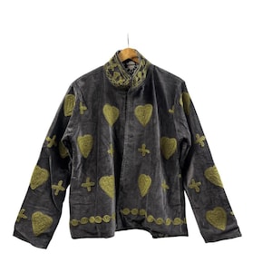 Puede incluir: Chaqueta de terciopelo gris oscuro con corazones, cruces y patrones circulares bordados en verde oliva. La chaqueta tiene cuello alto y mangas largas. El bordado es detallado y decorativo.