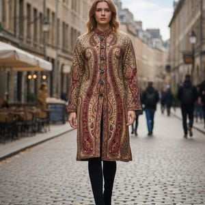 Könnte beinhalten: Ein langer Mantel mit Paisley-Muster in Braun-, Rot- und Goldtönen. Der Mantel hat eine Knopfleiste und wird mit schwarzen Leggings und Stiefeln getragen. Die Frau geht auf einer gepflasterten Straße.