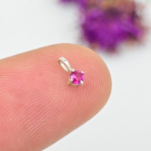 Op de afbeelding: Een kleine zilveren hanger met een helder roze edelsteen. De ronde edelsteen is gezet in een vier-klauwzetting en heeft een kleine lus aan de bovenkant voor een ketting. De hanger wordt getoond tegen een vage achtergrond.