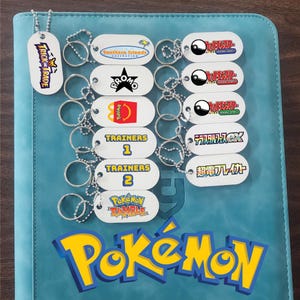 May include: A collection of white oval-shaped keychains with metal ball chains, each featuring various Pokémon-themed logos and text including Trick or Trade, Southern Islands, Promo, McDonald's, Trainers 1 and 2, Pokémon Rumble, and Japanese text.