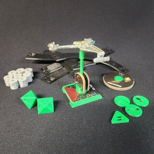 May include: A collection of miniature game pieces, including a silver spaceship model, green dice, and various tokens. The pieces are arranged on a dark surface, suggesting a tabletop game setting.