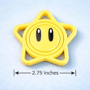 May include: A yellow star-shaped toy with a smiling face and black eyes. The toy measures 2.75 inches across. The star has a circular center and a star-shaped outline.
