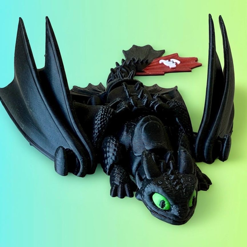 May include: A black 3D-printed dragon figurine with large wings and green eyes. The dragon has a red and white accent piece. The figurine is set against a gradient green and blue background.