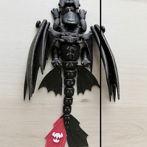May include: A black dragon figurine, approximately 8 inches in length, with articulated wings and tail. The tail features a red and white design. The dragon is posed on a light wood surface.