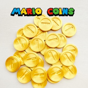 Könnte beinhalten: Eine Ansammlung goldfarbener Mario-Münzen mit erhabenem 'I'-Design, verstreut auf einer weißen Oberfläche. Der Text "MARIO COINS" ist in bunten Buchstaben darüber zu sehen. Diese Münzen sind wahrscheinlich für Spiele oder Cosplay gedacht.