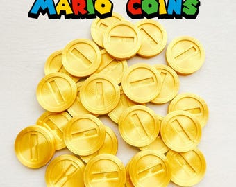 May include: A collection of gold-colored Mario Coins with a raised 'I' design, scattered on a white surface. The text "MARIO COINS" is displayed in colorful, block letters above the coins. These coins are likely for gaming or cosplay.
