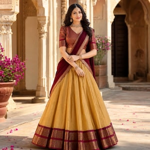 May include: A two-piece ensemble consisting of a short-sleeved, V-neck copper-toned blouse with ornate sleeve borders and a floor-length, pleated mustard-yellow skirt featuring a wide, intricate dark maroon border with gold-toned woven patterns.