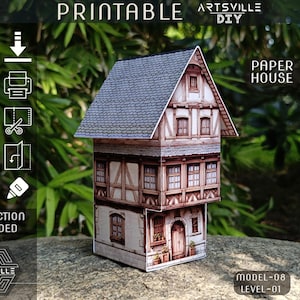 Puede incluir: Un detallado modelo de casa de papel con tejado gris, entramado de madera marrón y múltiples ventanas. El modelo está etiquetado como "Imprimible" e incluye instrucciones. También es visible el texto "Artsville DIY".