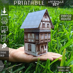 Puede incluir: Una casa de papel en miniatura con tejado de tejas grises y paredes con entramado de madera marrón se sostiene en una mano. La casa es un proyecto de bricolaje, con instrucciones incluidas. La imagen incluye el texto "Printable" y "Artsville DIY".