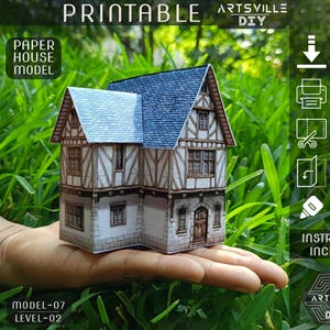 Op de afbeelding: Een papieren huismodel met een blauw dak en gedetailleerde gevel wordt in een hand gehouden. Het model is gelabeld met "Printable" en "Paper House Model". Instructies zijn inbegrepen voor het printen, knippen, vouwen en plakken van het model. De tekst "Artsville DIY" is ook zichtbaar.