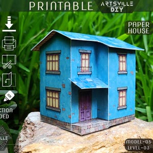 May include: A blue paper house model with a blue roof, windows, and a purple door. The model is labeled "Printable" and "Paper House". Instructions are included. The model is on a rock.